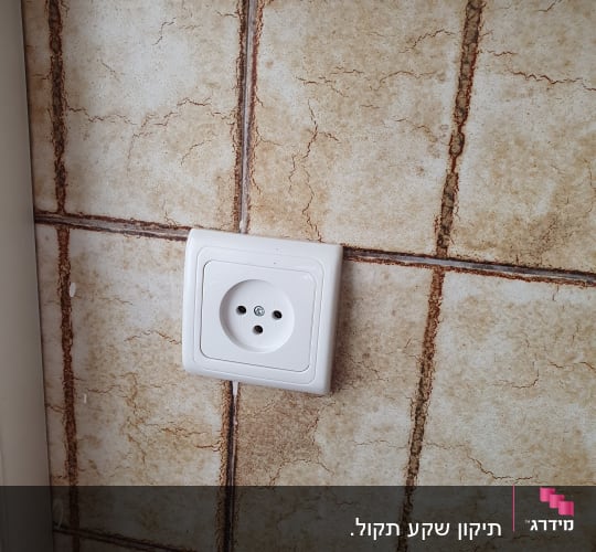 שקע חשמל לבן מותקן על קיר מרוצף